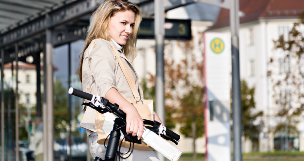 Frau mit Fahrrad an einer Haltestelle